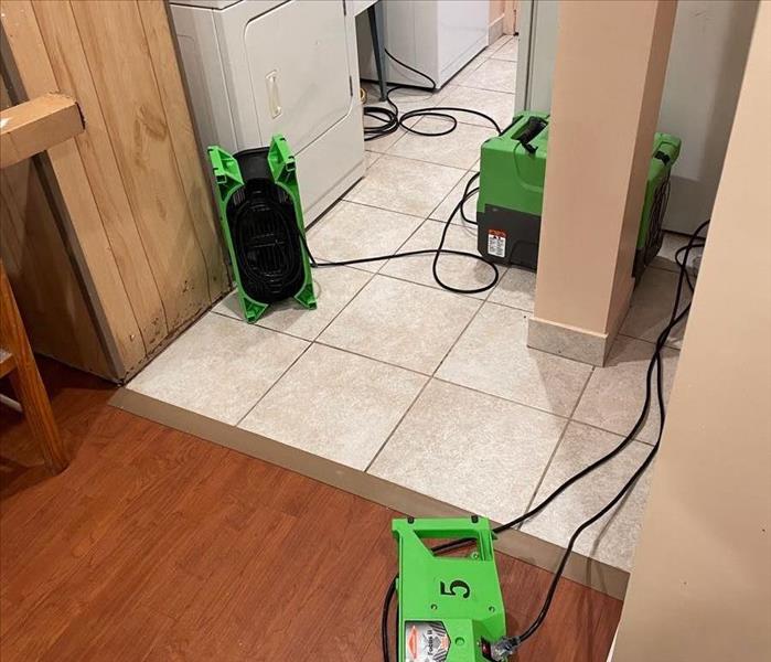 SERVPRO air movers and a dehumidifier positioned near a washer, dryer, and utility sink on wood and tile floors